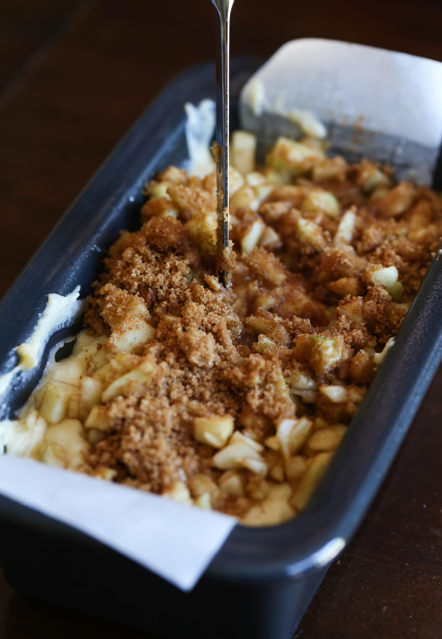 Swirling apple and cinnamon sugar into batter in a loaf pan.