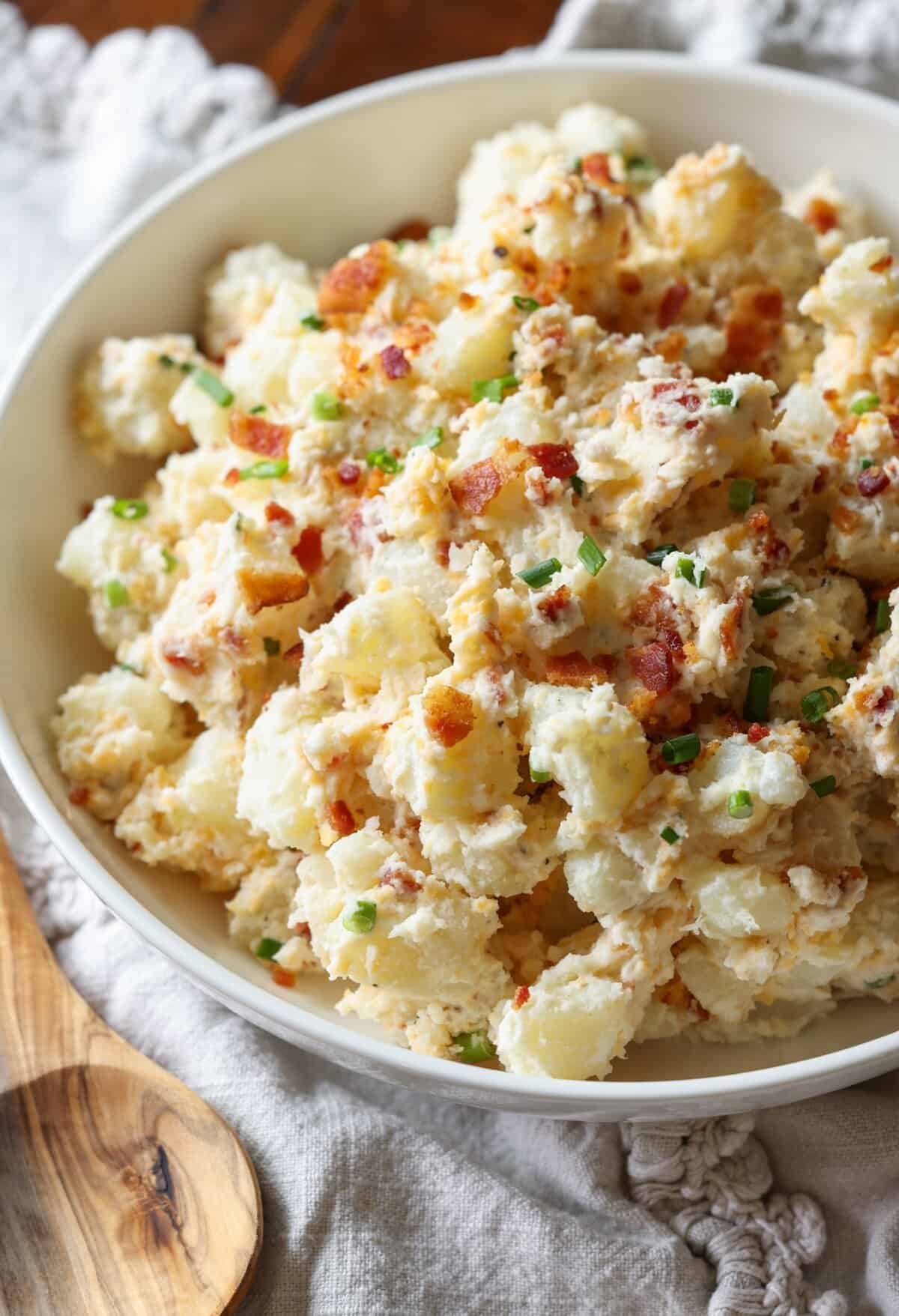 Loaded Baked Potato Salad is a classic potato salad recipe with a spin! All of your favorite baked potato flavors like bacon, cheddar cheese and chives make this a perfect BBQ side dish! A bowl of loaded baked potato salad with bacon and herbs