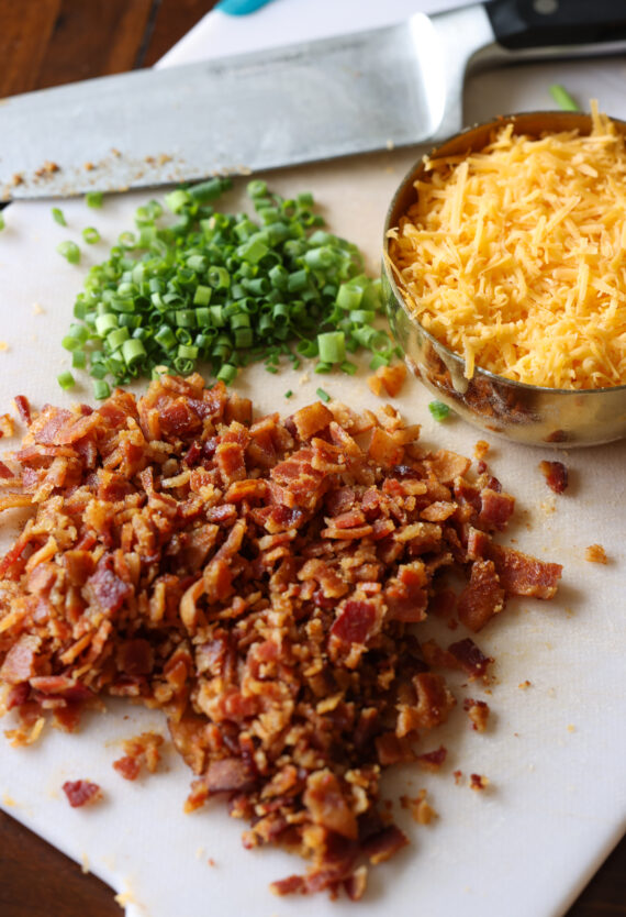 A cutting board with bacon, cheese, and green onions