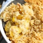 Top view of creamy squash casserole topped with crushed Ritz crackers in a baking dish with a serving spoon.