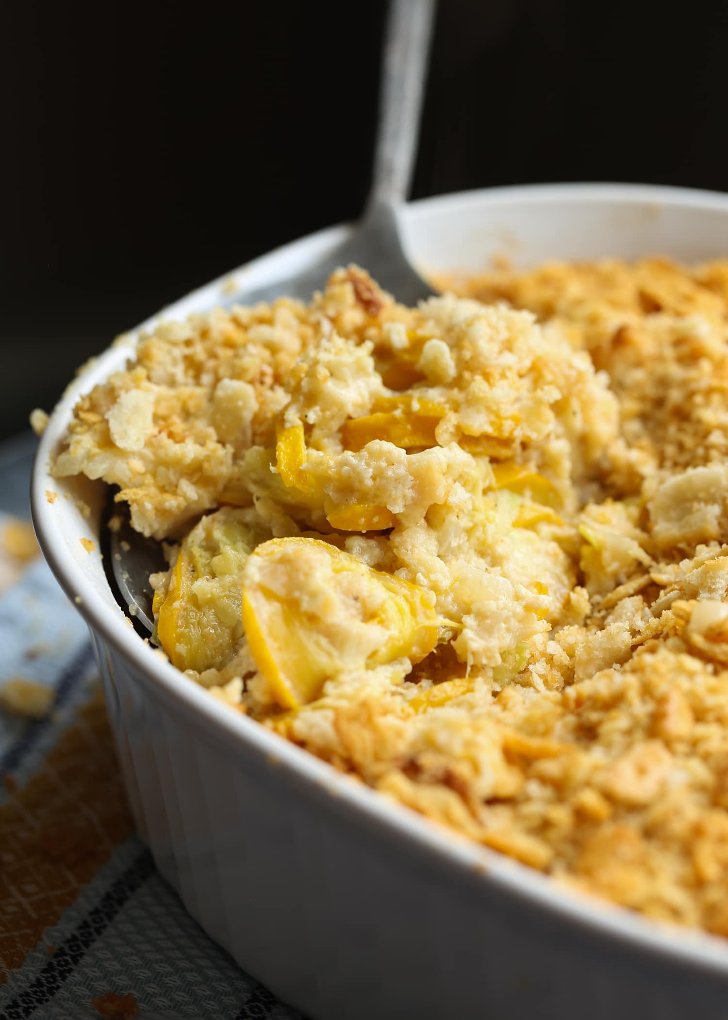 Creamy squash casserole topped with crushed Ritz crackers in a baking dish with a serving spoon.