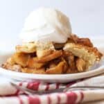 A slice of homemade apple pie on a white plate topped with a scoop of vanilla ice cream.