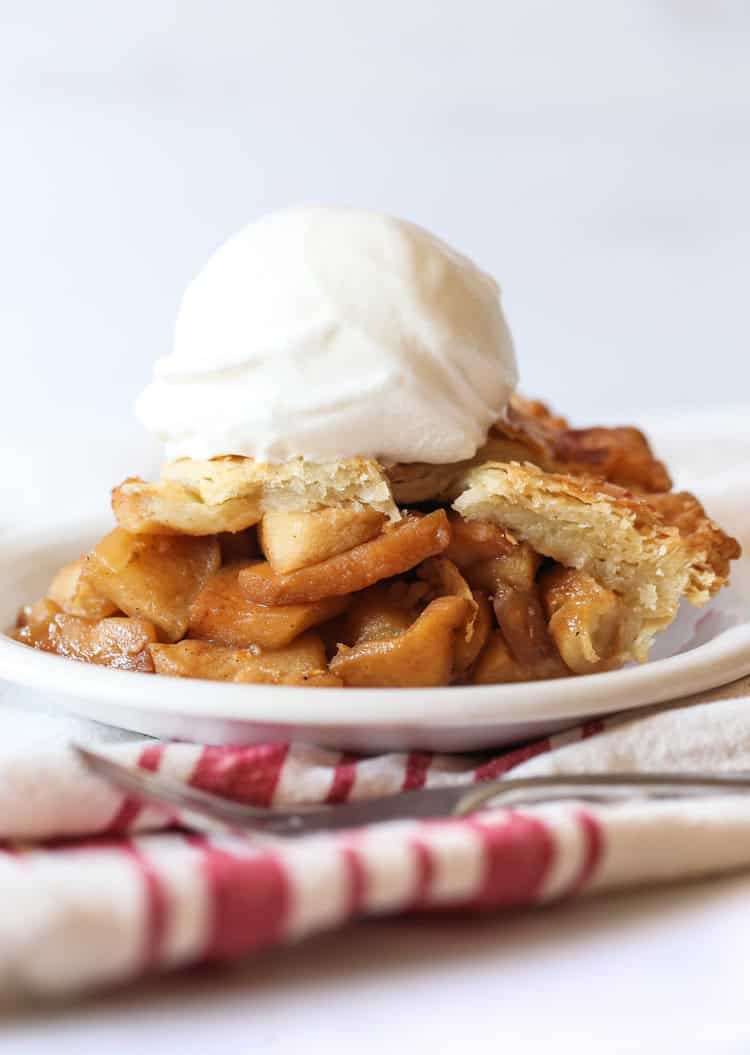 A slice of homemade apple pie on a white plate with a scoop of vanilla ice cream.