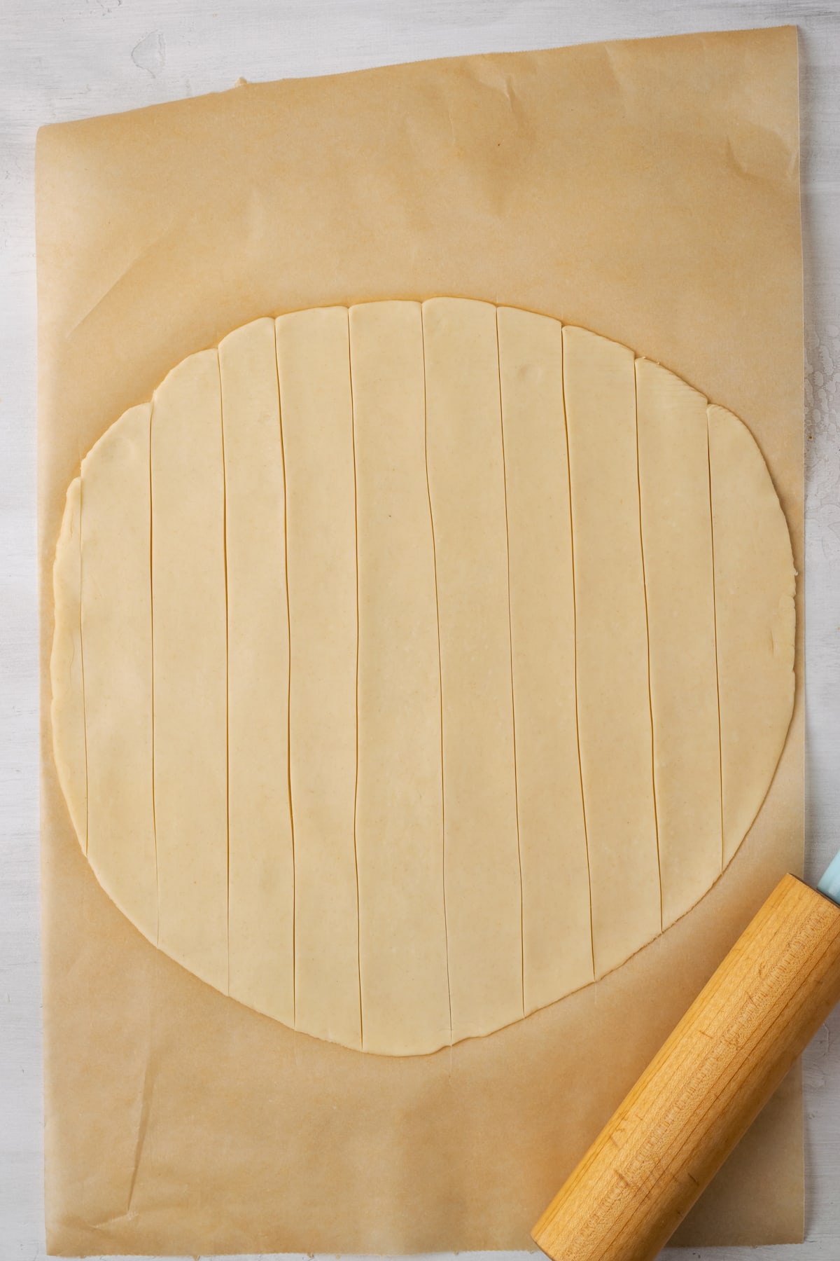 A round, rolled out pie crust on a piece of parchment paper, cut into strips for the lattice crust.