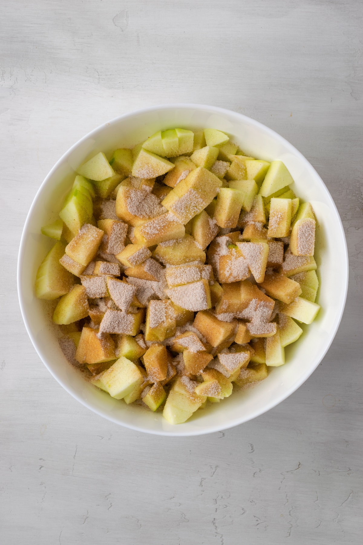 Apple slices covered with cinnamon sugar in a large white bowl.
