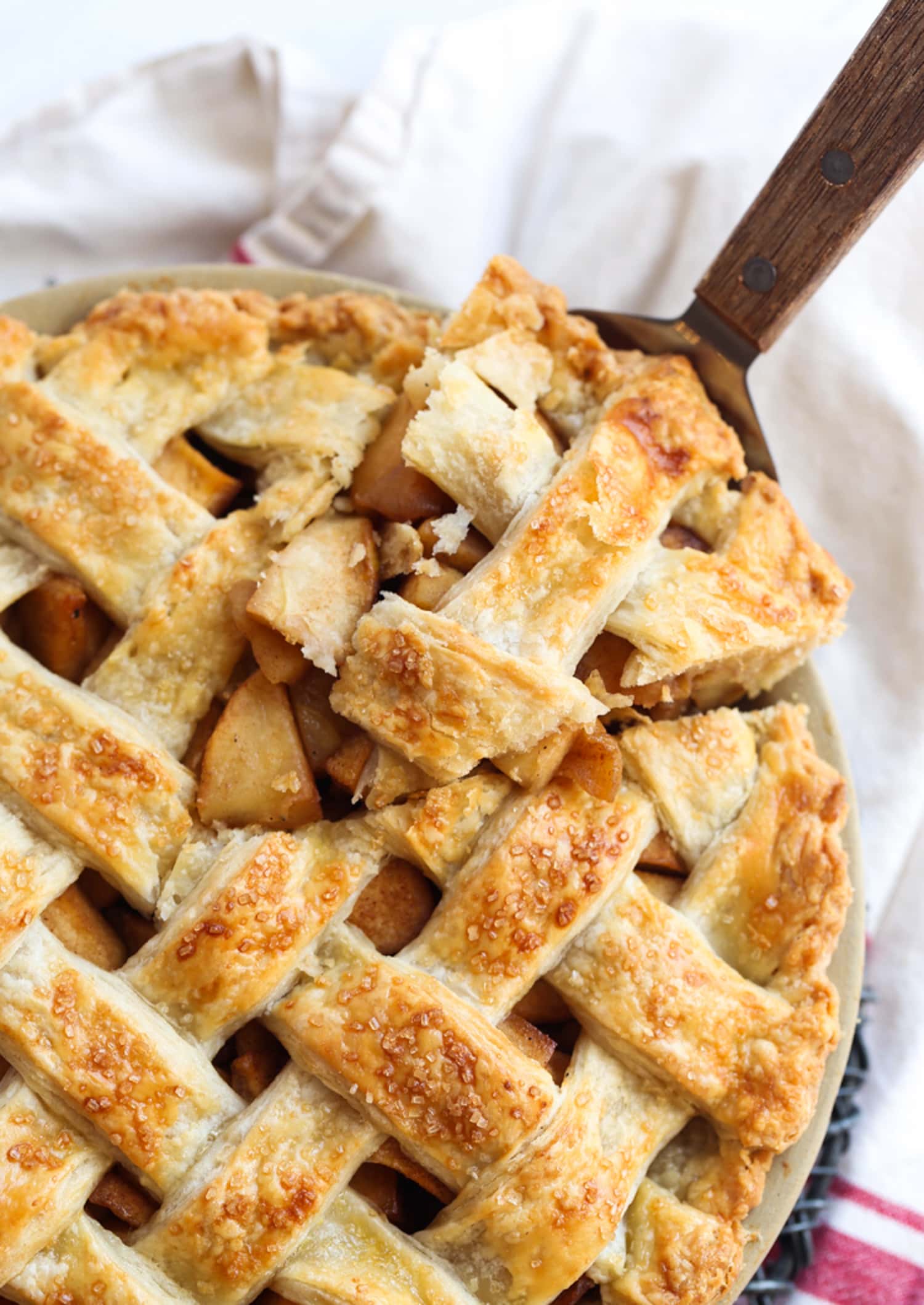 A slice of apple pie with a lattice crust lifted from a full pie in a pie plate.