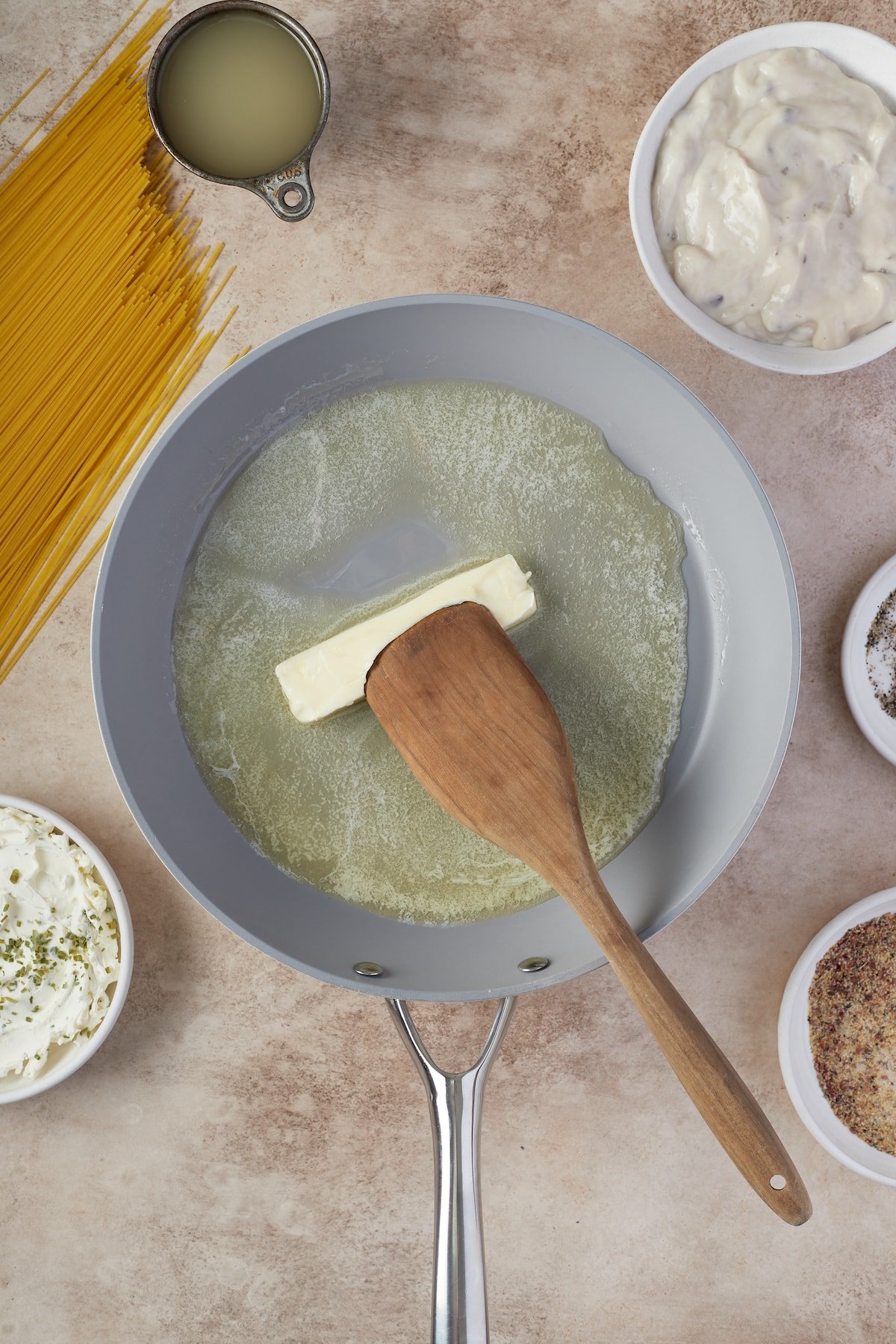 A wooden spoon is used to push butter around a sauce pan as it melts.