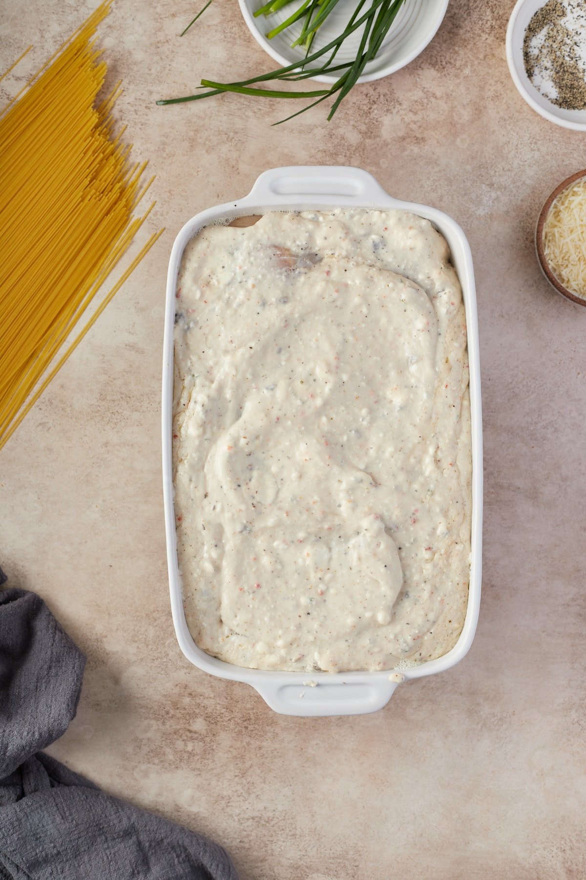 Cream cheese sauce poured over chicken breasts in a baking dish.
