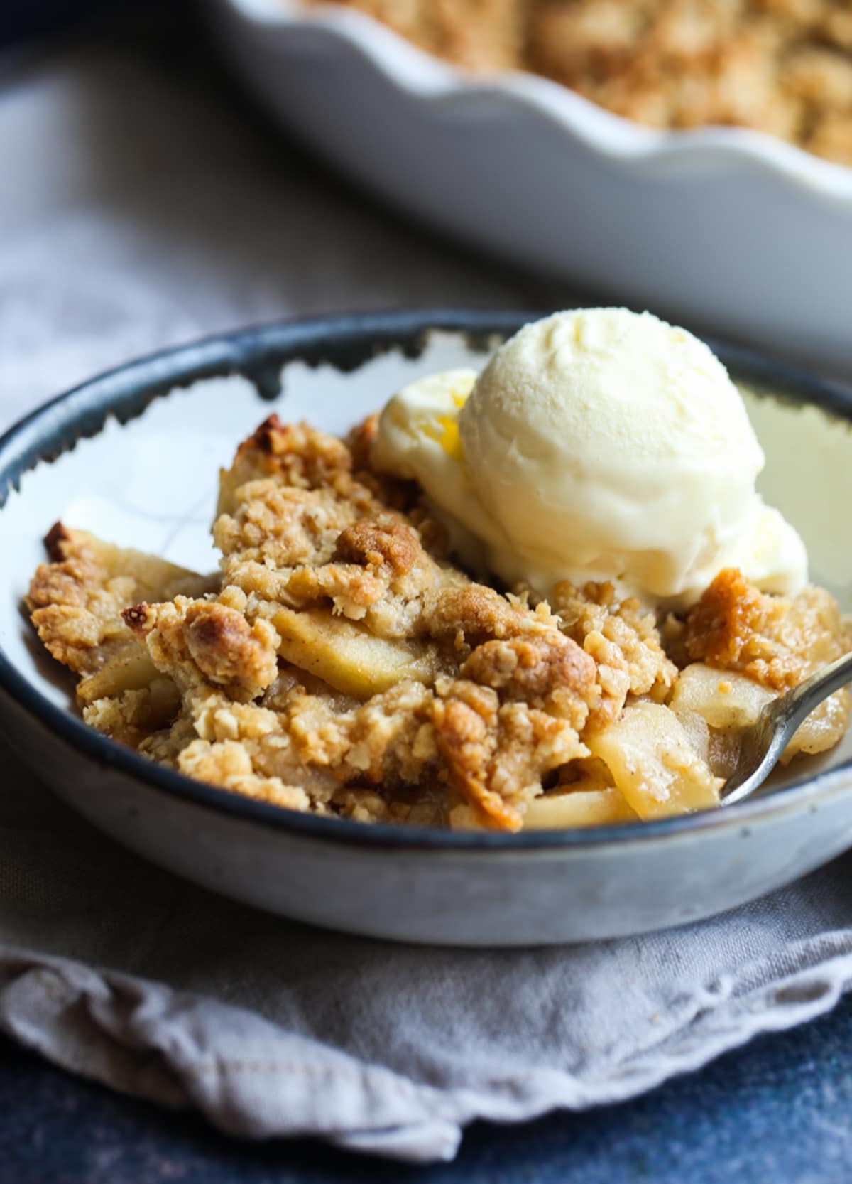 Apple crisp portion in a bowl with a spoon and a scoop of ice cream