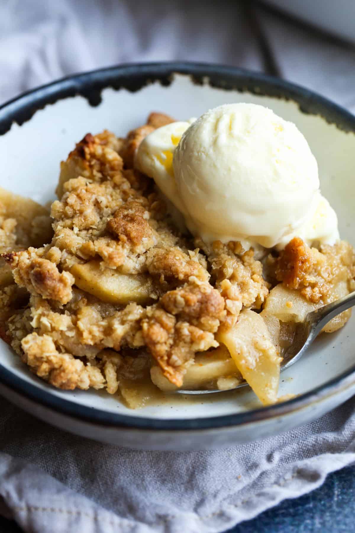 Apple crisp served in a ceramic bowl with a scoop of ice cream