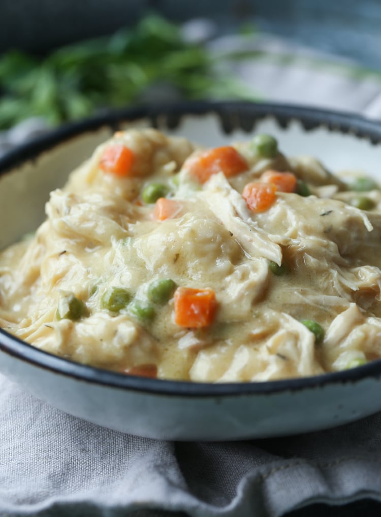A bowl of chicken and dumplings with peas and carrots