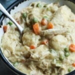 A bowl of creamy chicken and dumplings with carrots and peas in a bowl with a spoon