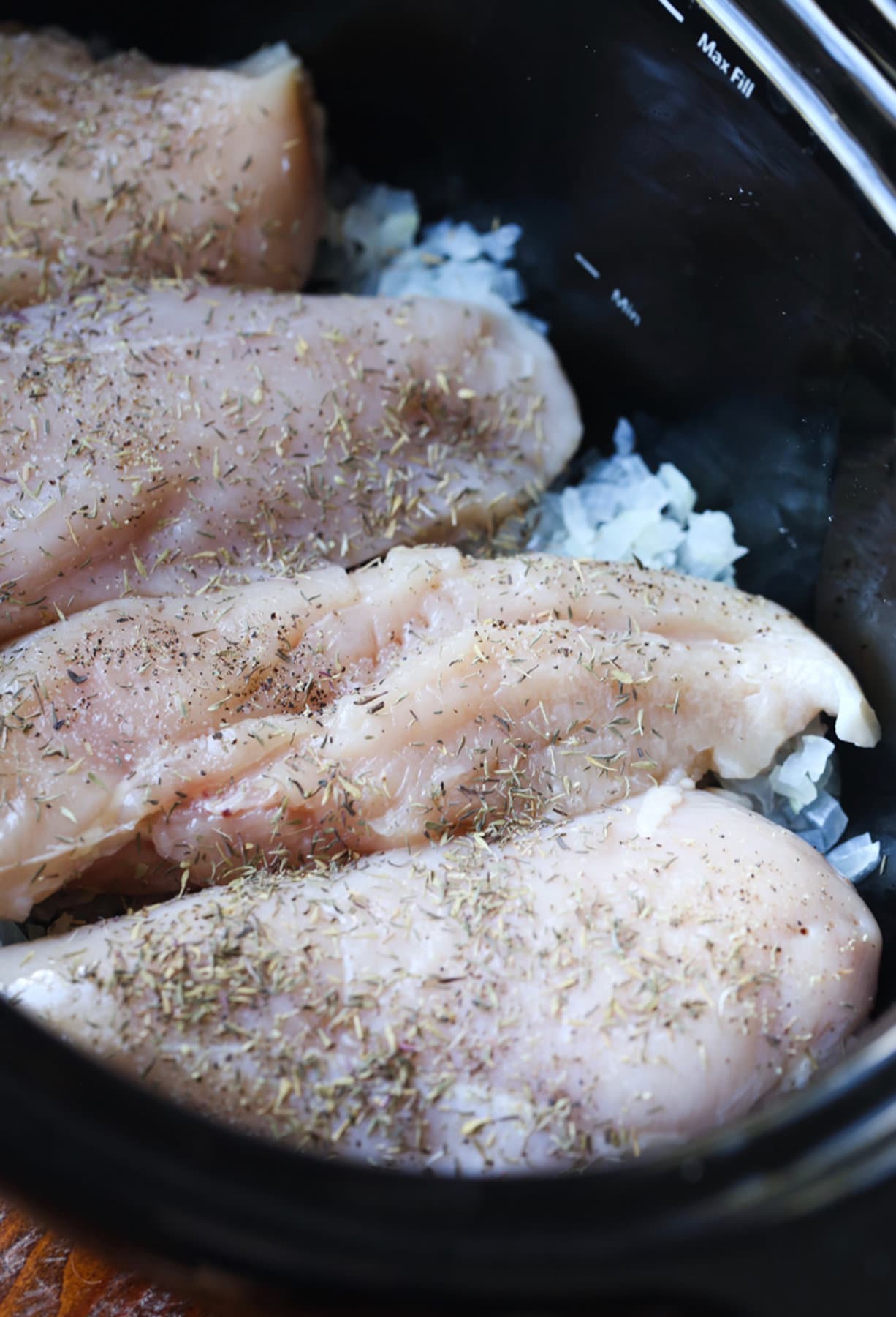 Four raw chicken breasts in a slow cooker