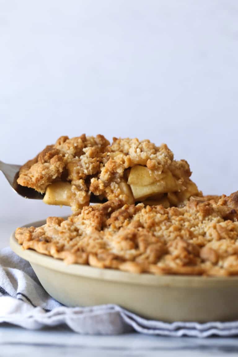 Serving a slice of Dutch apple pie from the rest of the pie on a pie plate.