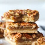 Three stacked Pecan Pie Bars showing the shortbread crust layer, the filling and nuts layers with a bite taken from the bar on top.