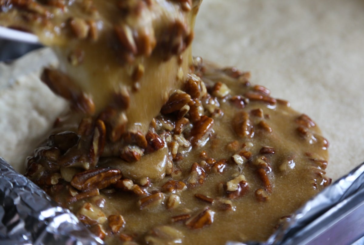 Pouring pecan pie filling onto a shortbread crust making pecan pie bars