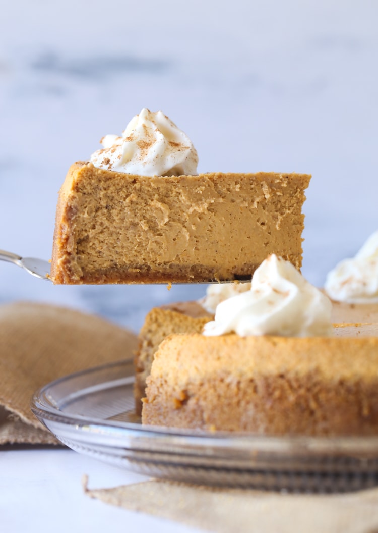 A slice of pumpkin cheesecake is lifted from a cake on a platter.
