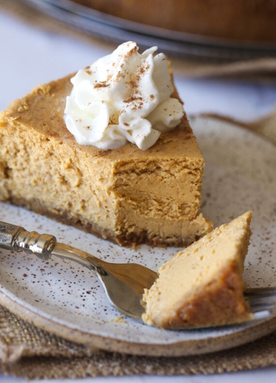 Pumpkin Pie Cheesecake with a bite taken out on a plate with whipped cream.