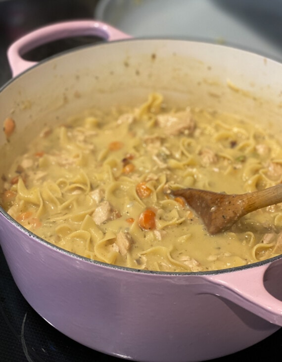 A large Dutch oven cooking down broth and noodles for creamy chicken and noodles recipe