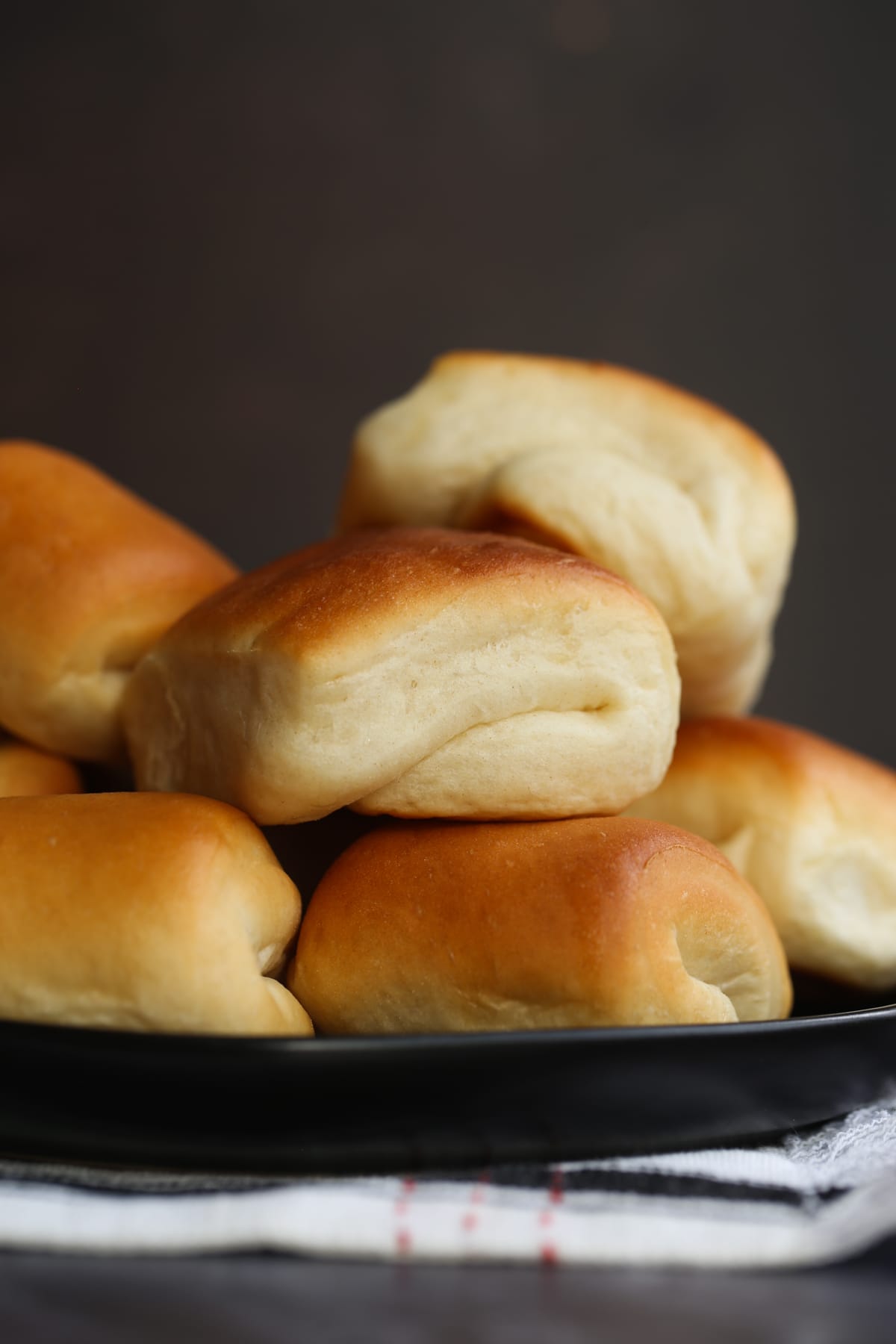 Side view of golden baked Parker House rolls piled on a black plate.