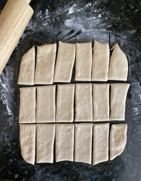 Yeasted dough rolled out and cut into rectangles on a floured surface, next to a rolling pin.