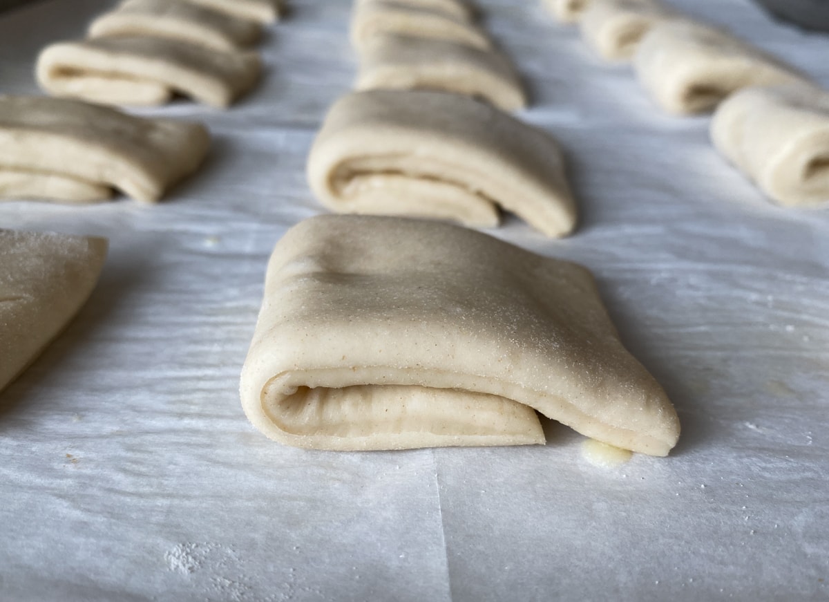 Unbaked Parker House rolls on a parchment-lined baking sheet.