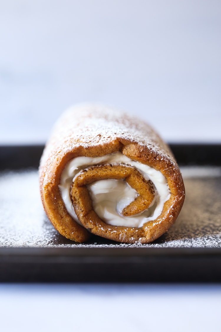 View from the front of a pumpkin roll stuffed with cream cheese frosting, and dusted in powdered sugar