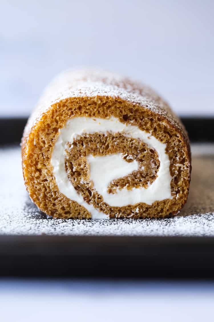 Head-on view of a pumpkin roll dusted with powdered sugar.
