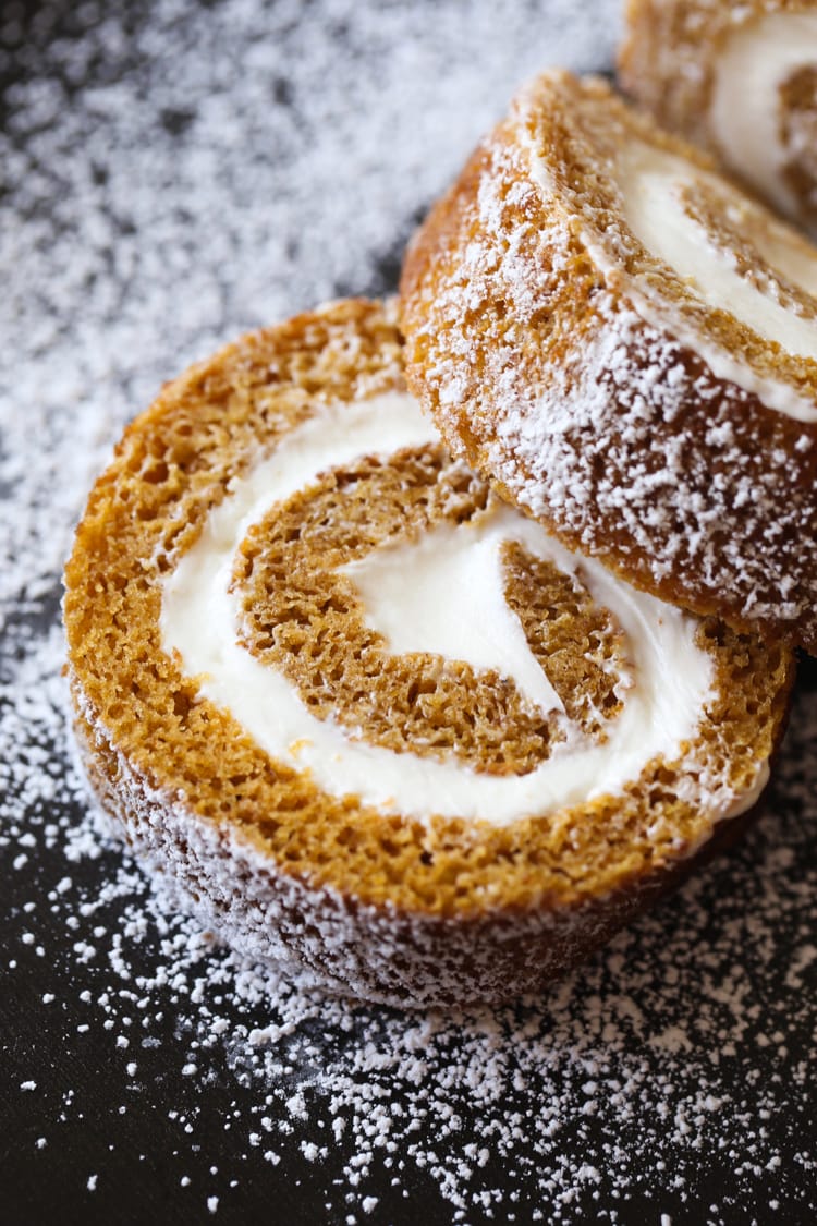 Two slices of a pumpkin roll filled with cream cheese frosting, on a plate, dusted with powdered sugar