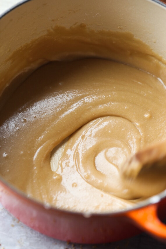 Close up of a wooden spoon stirring brown sugar icing in a pot.