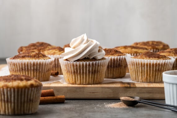 A snickerdoodle cupcake topped with a swirl of cinnamon frosting, with unfrosted cupcakes in the background.