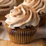 Snickerdoodle cupcakes topped with swirls of cinnamon buttercream frosting on a wooden cutting board.