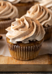 Snickerdoodle cupcakes topped with swirls of cinnamon buttercream frosting on a wooden cutting board.