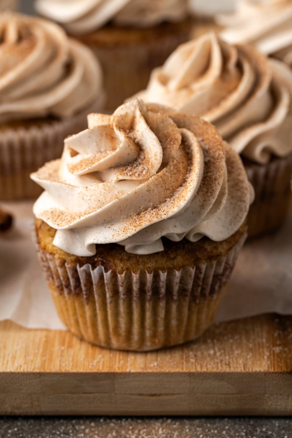 Snickerdoodle cupcakes topped with swirls of cinnamon buttercream frosting on a wooden cutting board.