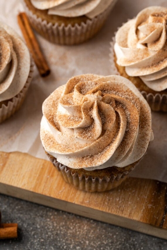 Snickerdoodle cupcakes topped with swirls of cinnamon buttercream frosting on a wooden cutting board.