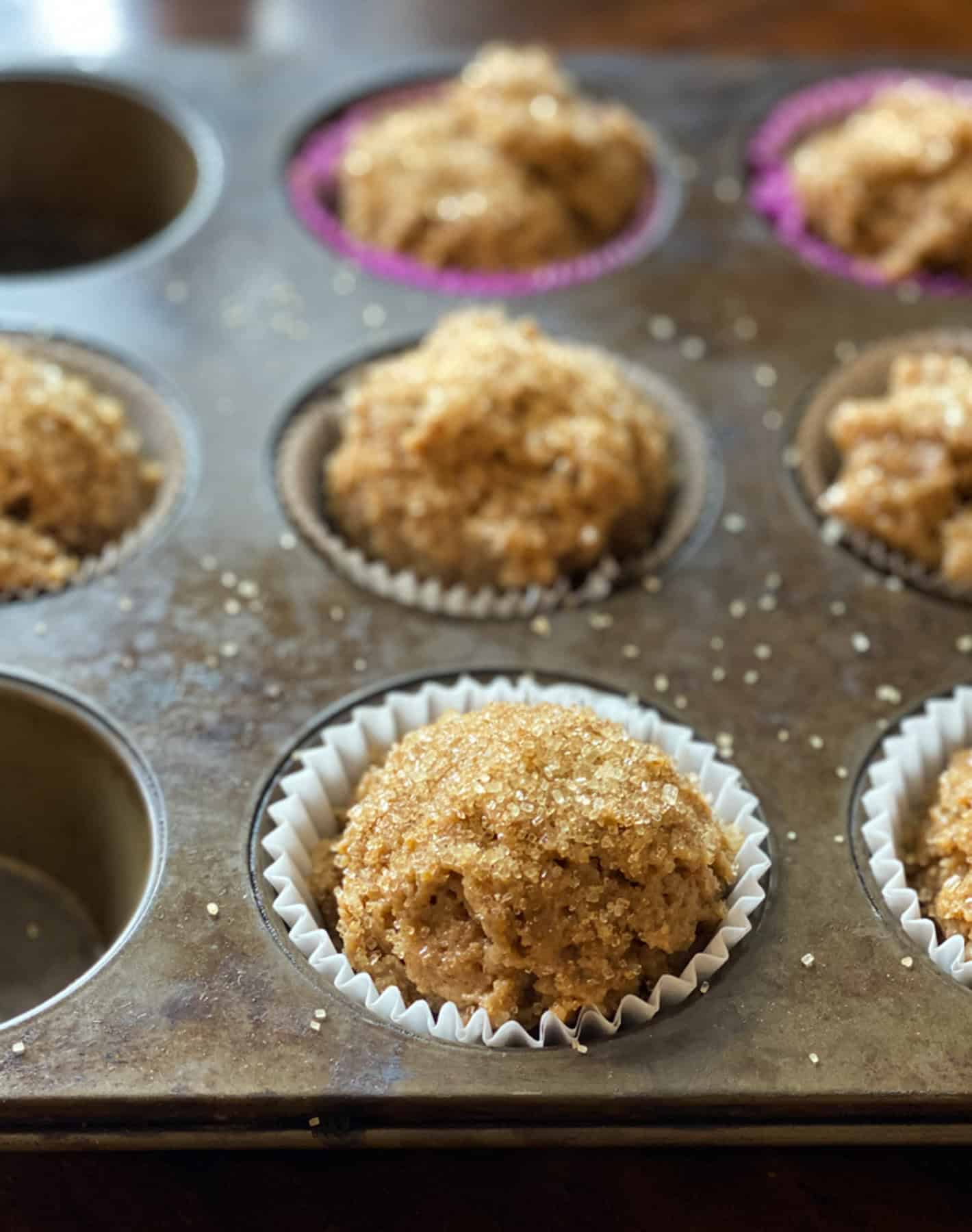 Bran muffin batter topped with turbinado sugar in a lined muffin pan.