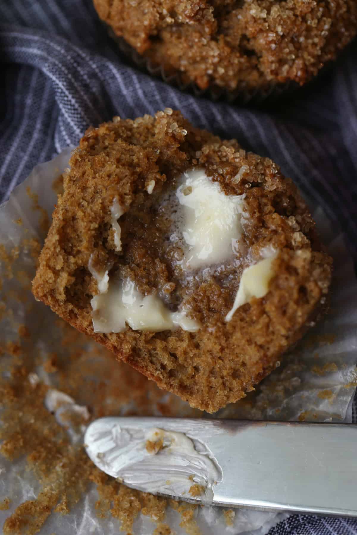 Close up of one half of a bran muffin spread with butter next to the tip of a butter knife.