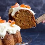 A slice of carrot bundt cake being lifted from the rest of the frosted cake on a plate.