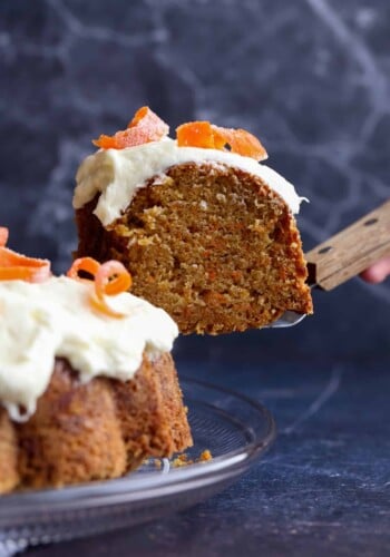 A slice of carrot bundt cake being lifted from the rest of the frosted cake on a plate.