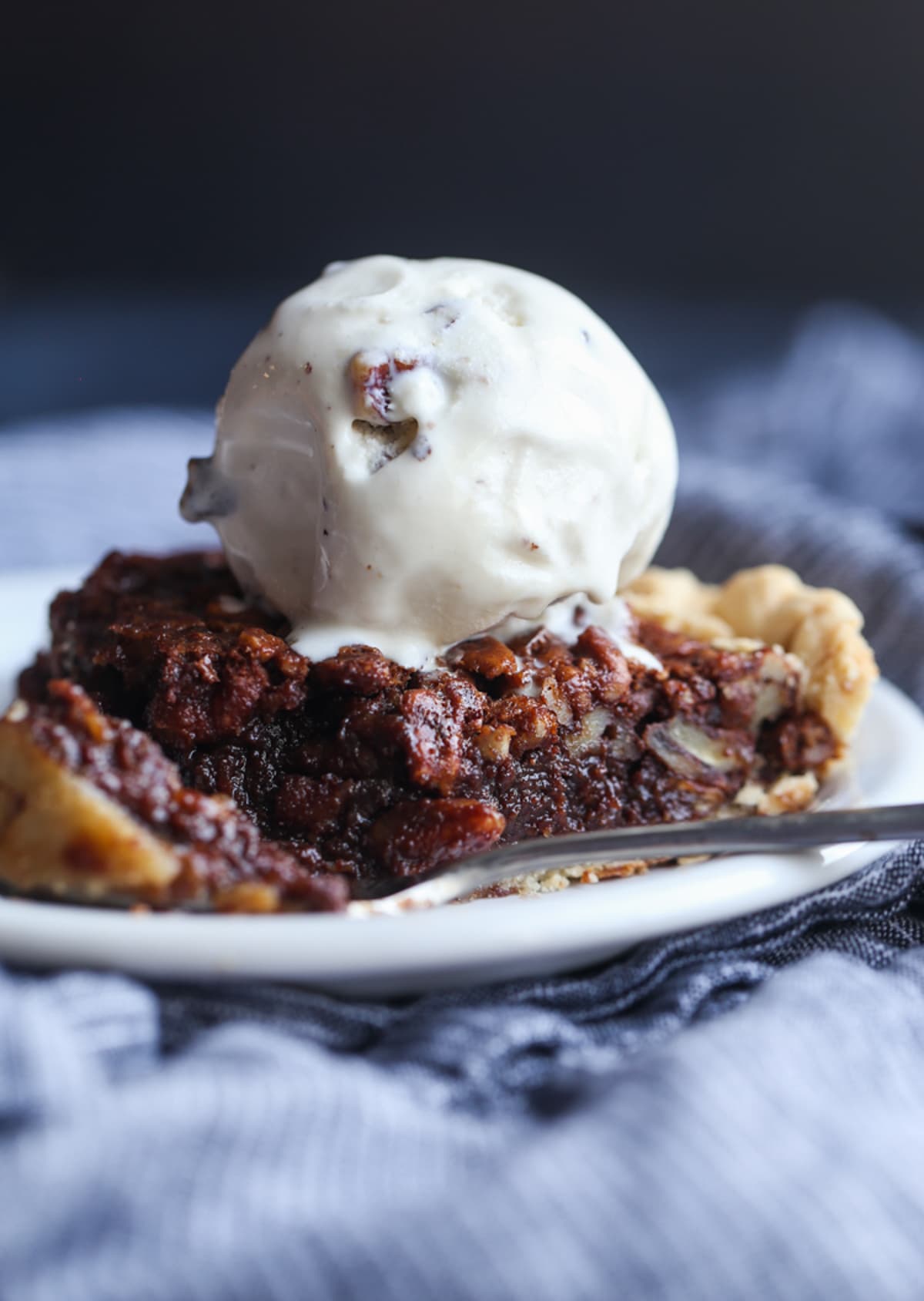 A slice of chocolate pecan pie on a plate of vanilla ice cream with a fork removed.