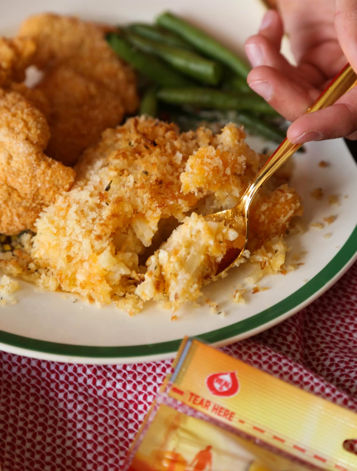 Close up of a hand taking a spoonful of casserole from a dish with green beans and chicken.