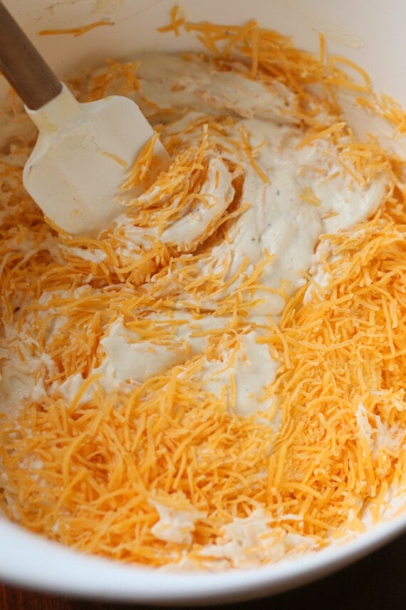 A mixing bowl with shredded cheese on top of cream of chicken soup, with a rubber spatula.