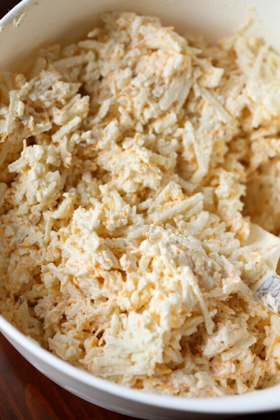Close up of shredded cheese, hash browns, cream of chicken soup, sour cream, and seasonings mixed together in a bowl.