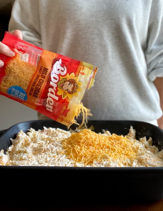 A bag of shredded cheese being poured over the top of an unbaked casserole.