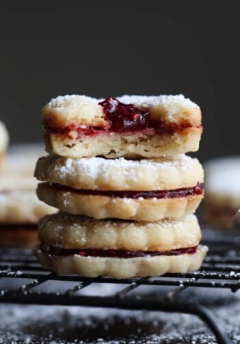 Linzer cookies filled with strawberry preserves stacked with the top one broken in half