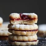 Linzer cookies filled with strawberry preserves stacked with the top one broken in half