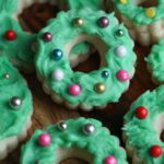 Assorted Christmas wreath cookies decorated with green frosting and colorful ball sprinkles.