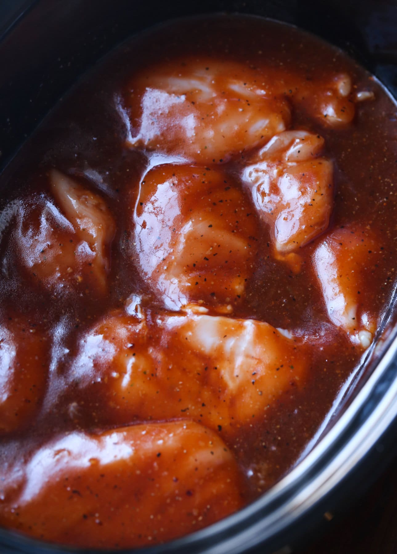 pollo crudo en una olla de cocción lenta cubierta con salsa BBQ
