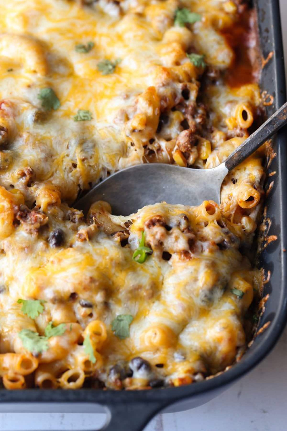 Baked chili mac and cheese in a black casserole dish with a spoon tucked into the corner.
