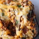 A spoon lifting a serving of chili mac and cheese from a black casserole dish.